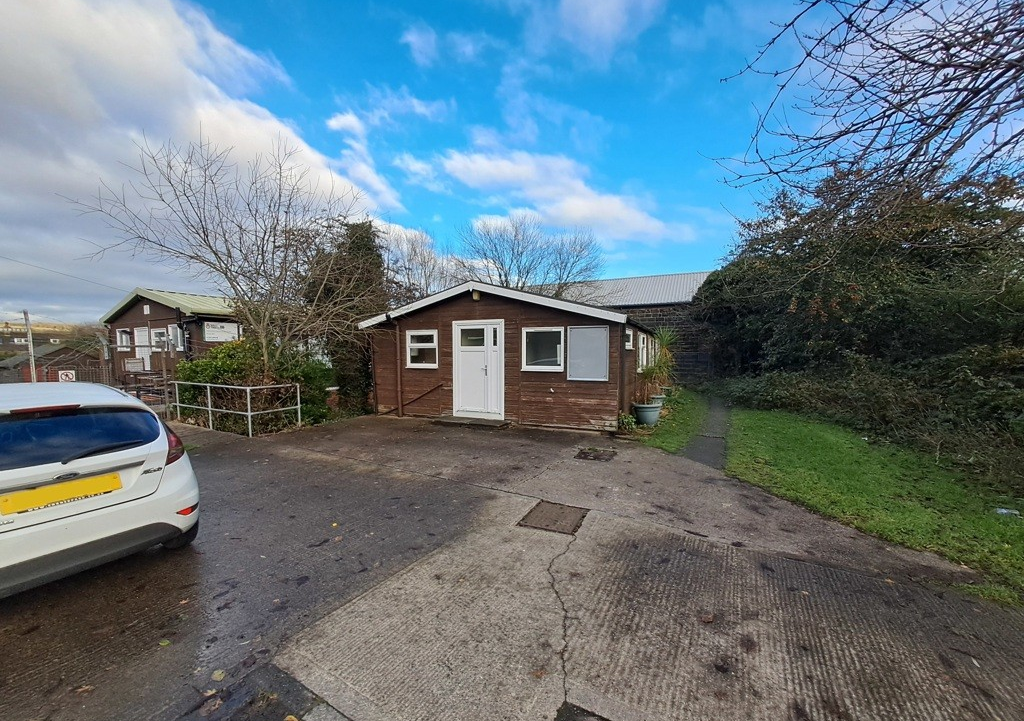 Wooden hut single-storey building with a flat area of concrete hardstanding to the front, grass and a small footpath designated a public right of way to the right