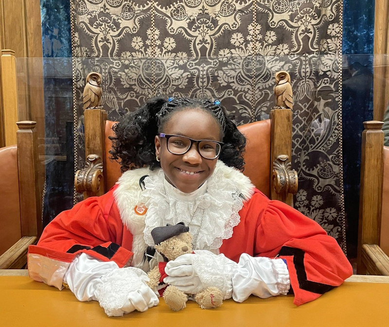 Young girl smiling sat in a big chair holding a teddy bear