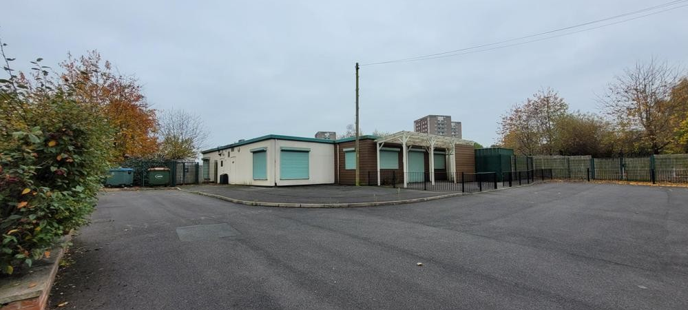 Green grass and tarmac driveway in front of a one storey building with green window shutters